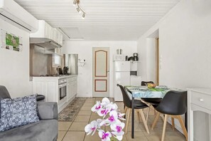 A compact kitchen with white cabinets, a dining area with a table and chairs, and a sofa with a patterned cushion. - Homerez - Holiday Apartment in Vidauban (Vidauban)