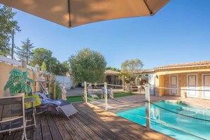 A wooden deck with a pool, a volleyball net, and a statue.