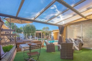 A covered outdoor area with a pool, wicker furniture, and a table.