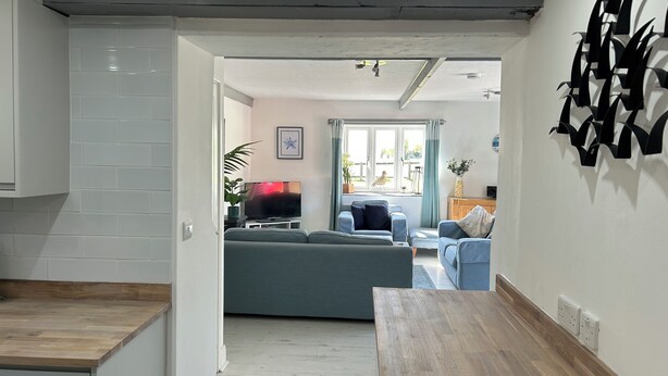 A modern living room with a sofa, a TV, and a dining area with a wooden table. - Stables, quality 3 bed character cottage,  views across golf course to the sea (Bude)