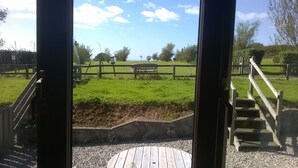 A view through a window of a grassy area with a wooden fence, a sign, and a staircase leading outside. - Stables, quality 3 bed character cottage,  views across golf course to the sea (Bude)