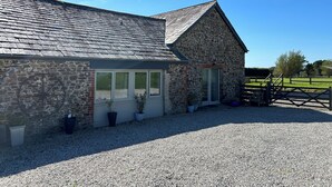 A stone building with a sloped roof, a gravel driveway, and a wooden fence. - Stables, quality 3 bed character cottage,  views across golf course to the sea (Bude)