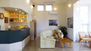 Un área de recepción con mostrador, un sofá, una silla, una mesa y un osito de peluche.