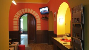 A kitchen with a TV mounted on the wall, a refrigerator, and a dining area with a table and chairs. - Traveler's Hostel & Apartments (Belgrade)