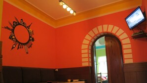 A room with a red wall, a round mirror, a television, a wooden door, and a seating area with a table and cushions. - Traveler's Hostel & Apartments (Belgrade)