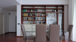 A modern living room with a glass dining table, four chairs, and a large bookshelf filled with books. - Italianway - San Bartolomeo 7 (Rapallo)