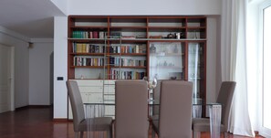 Ein Zimmer mit Bücherregal, zwei Stühlen, einem Glastisch und einer Tür.
