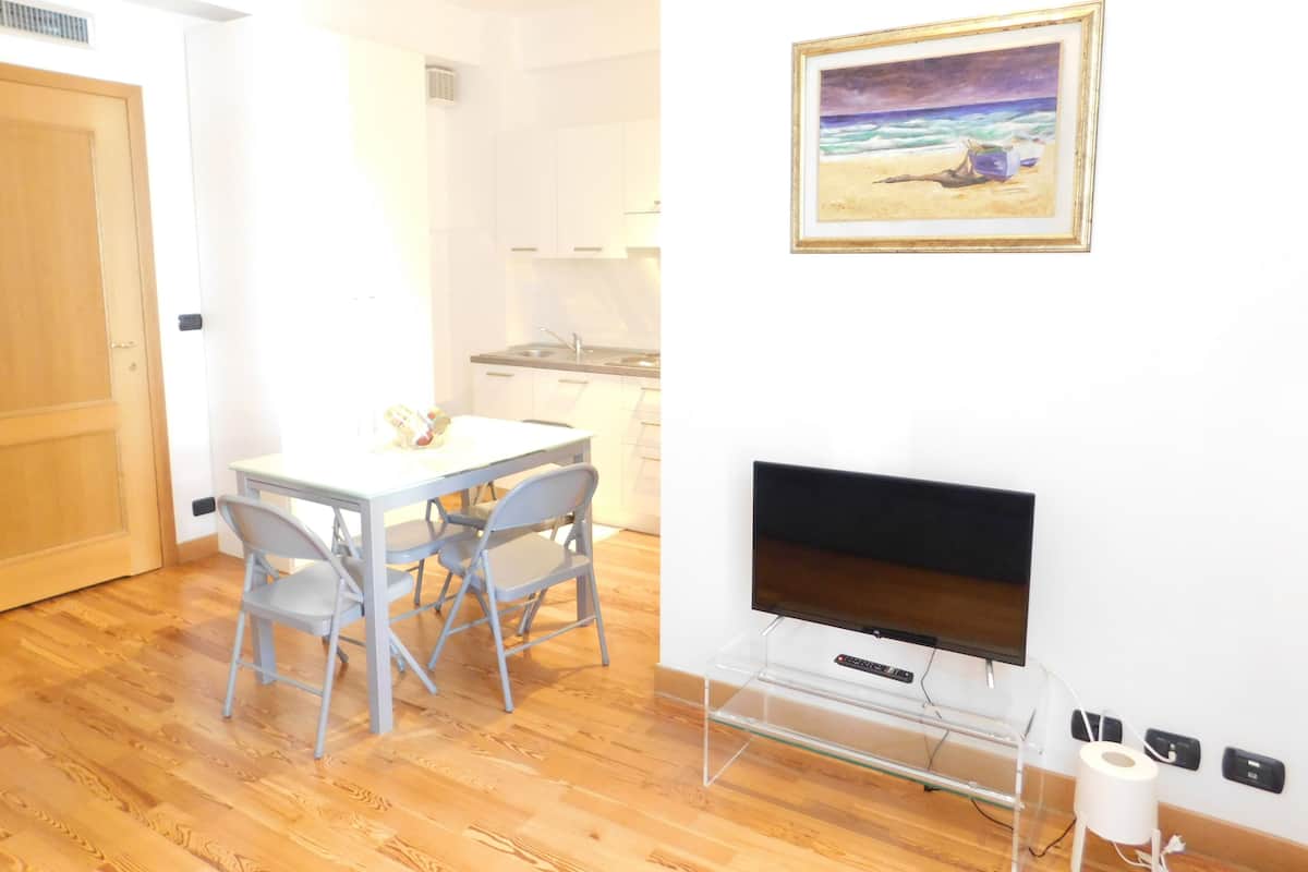 Un espace de vie compact comprenant un coin repas, une kitchenette et un téléviseur fixé au mur.