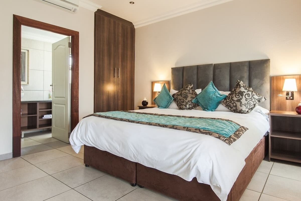 Habitación de hotel con una cama grande, dos mesitas de noche con lámparas, un armario y un baño visible a través de una puerta abierta.