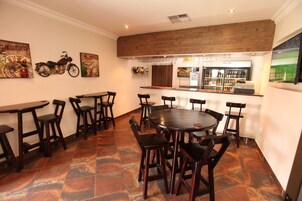 Un restaurante con zona de bar, mesas y sillas de madera y suelo de baldosas.