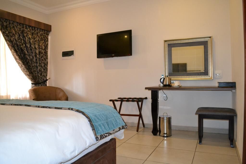 A hotel room with a bed, a desk, a chair, a TV, a mirror, and a trash can.