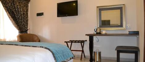 A hotel room with a bed, a desk, a chair, a TV, a mirror, and a trash can.