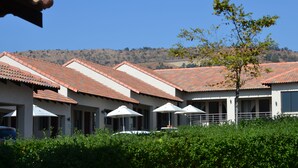 Eine Reihe von Hotelzimmern mit roten Ziegeldächern, Sonnenschirmen und Blick auf einen Hügel.
