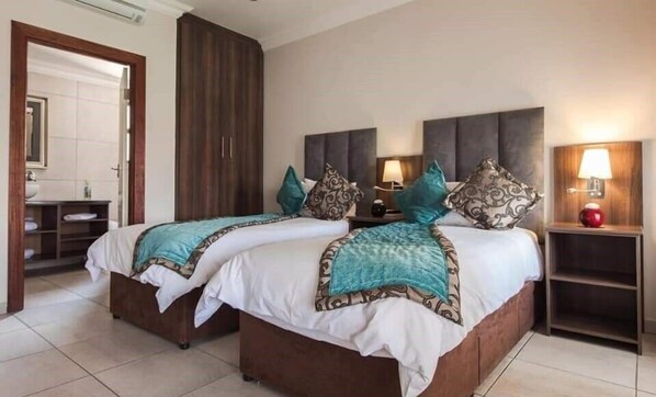 A hotel room with two beds, a bathroom, and a nightstand with a lamp.