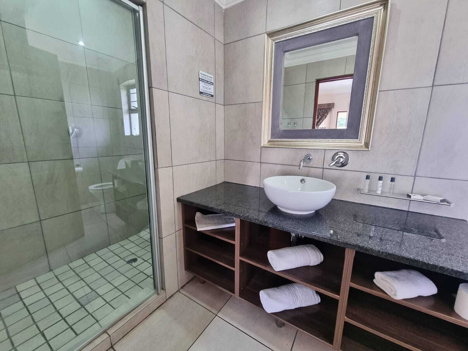 A modern bathroom with a glass shower enclosure, a white sink, and a vanity with towels.