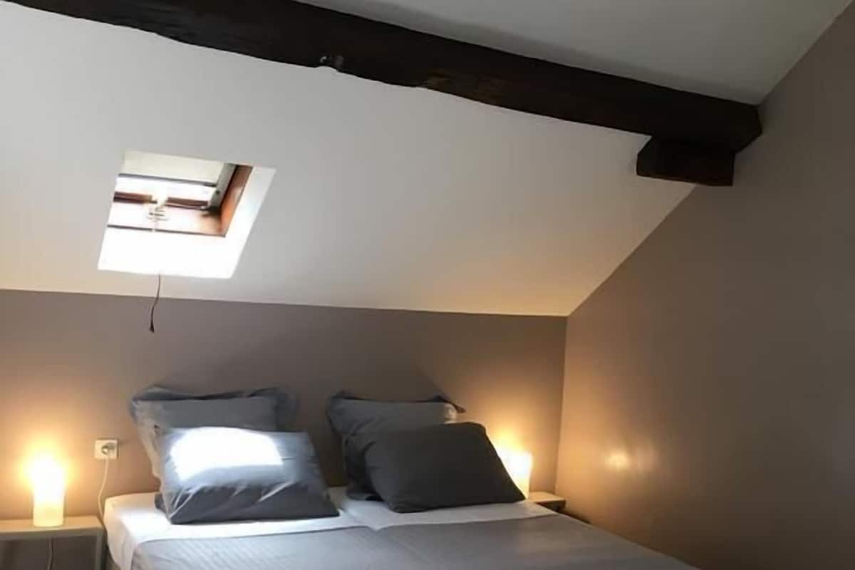 A bedroom with a bed, bedside lamps, a skylight, and a tiled floor.