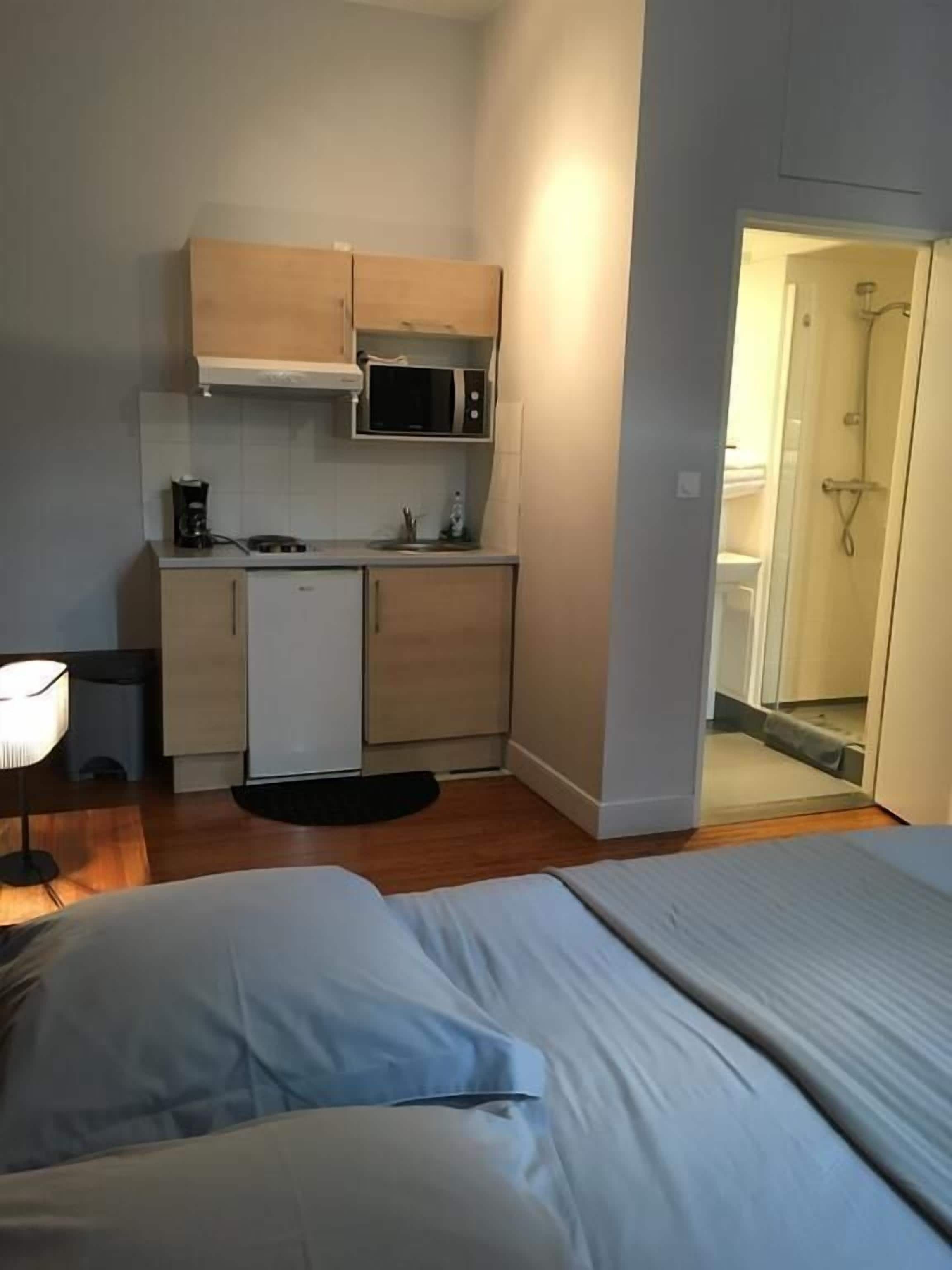 Una habitación de hotel compacta con kitchenette, cama y zona de ducha.