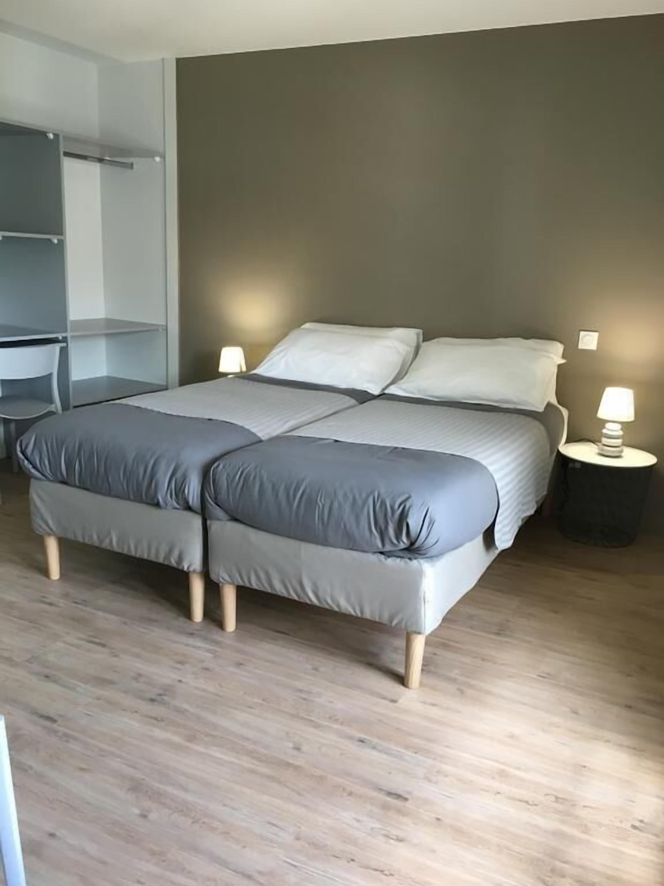 A double bed with grey bedding, a bedside table with a lamp, and a wardrobe.