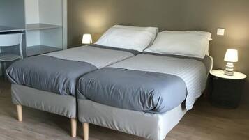 Una cama doble con ropa de cama gris, una mesita de noche con lámpara y un armario.