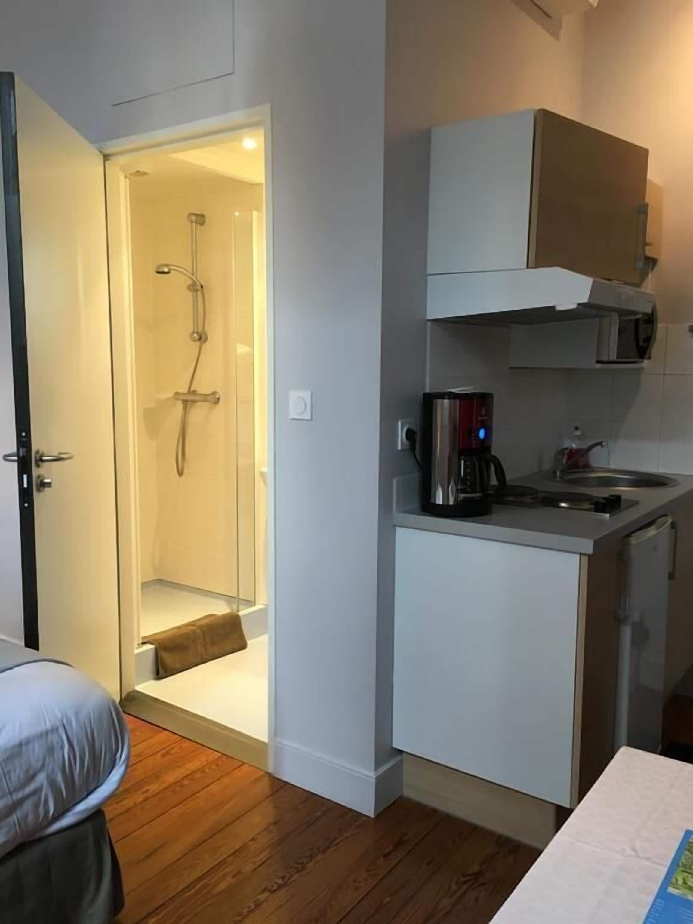 A compact hotel room with a shower, a kitchenette, and a bed.
