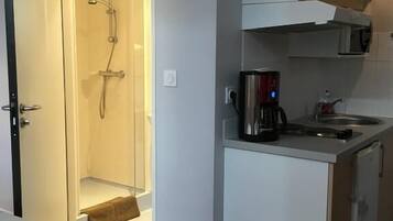 A compact hotel room with a shower, a kitchenette, and a bed.