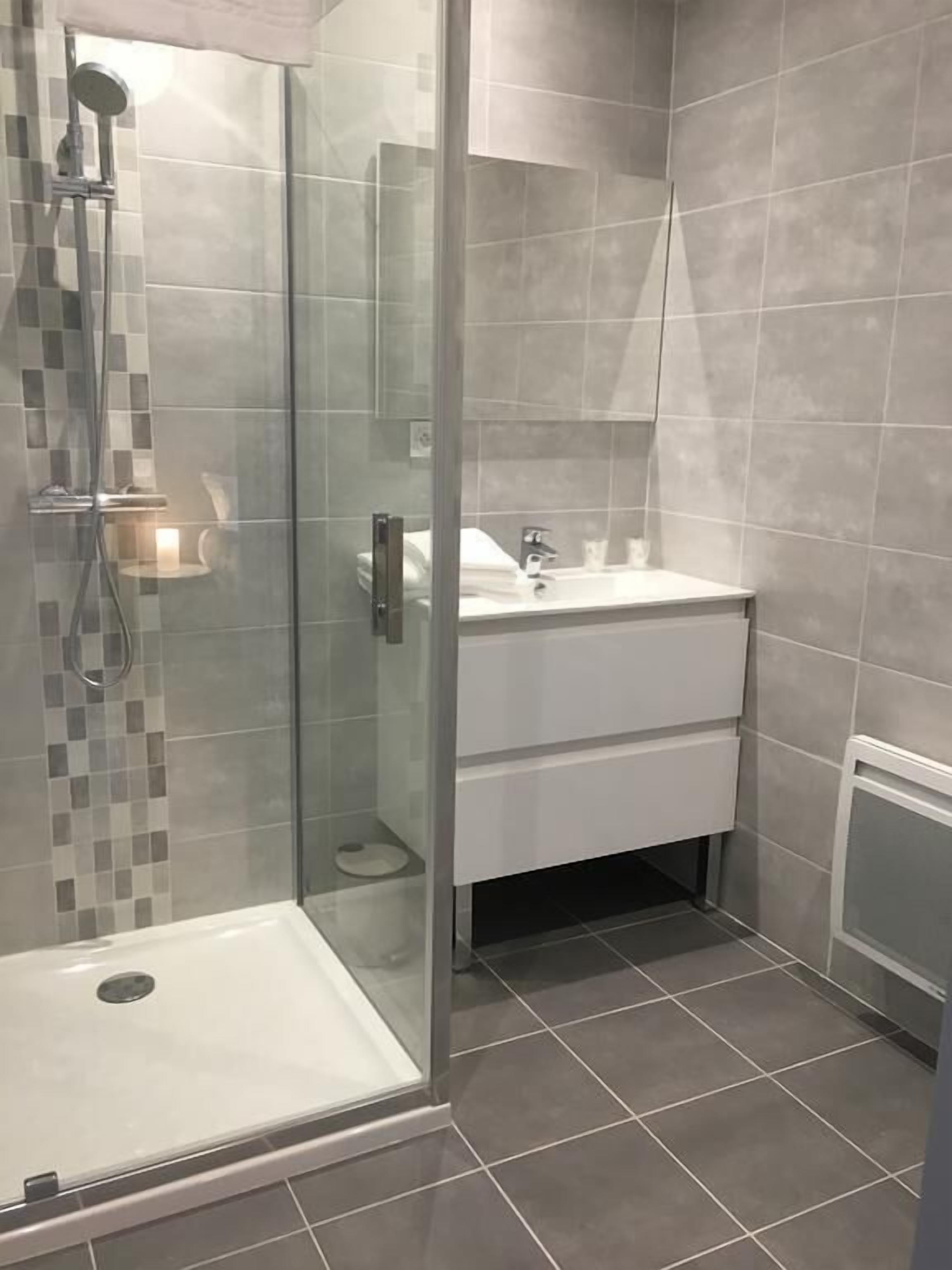 A modern bathroom with a glass shower enclosure, a white sink, and a tiled floor.