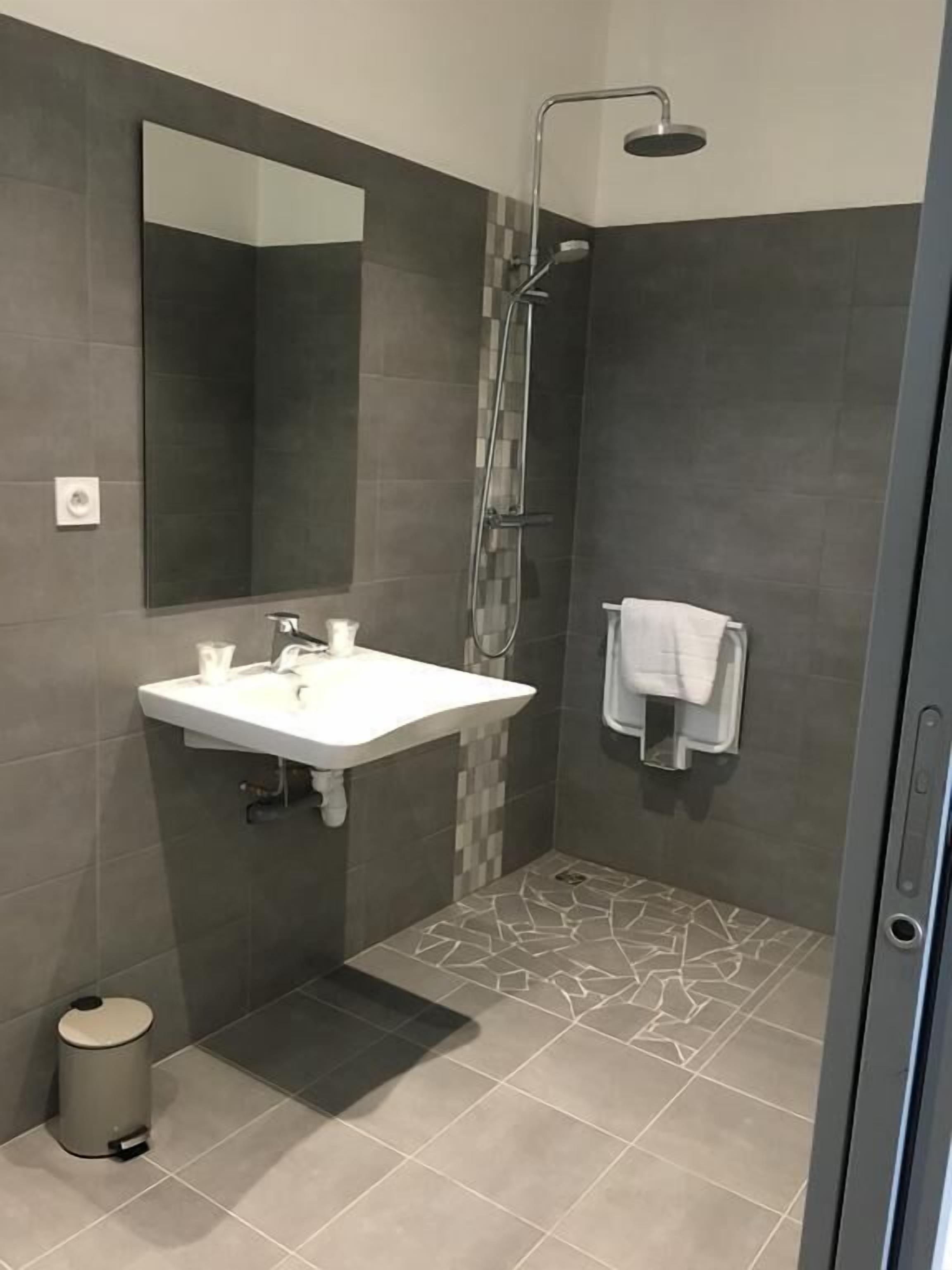 A modern bathroom with a large mirror, a white sink, a shower, and a towel rack.