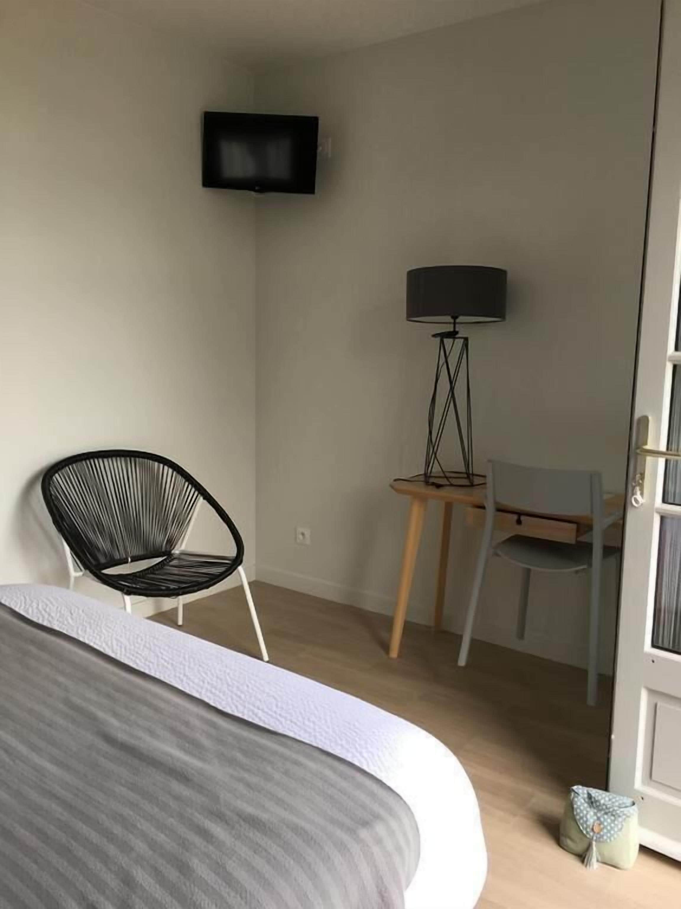 A bedroom with a bed, a black chair, a desk with a lamp, and a TV mounted on the wall.