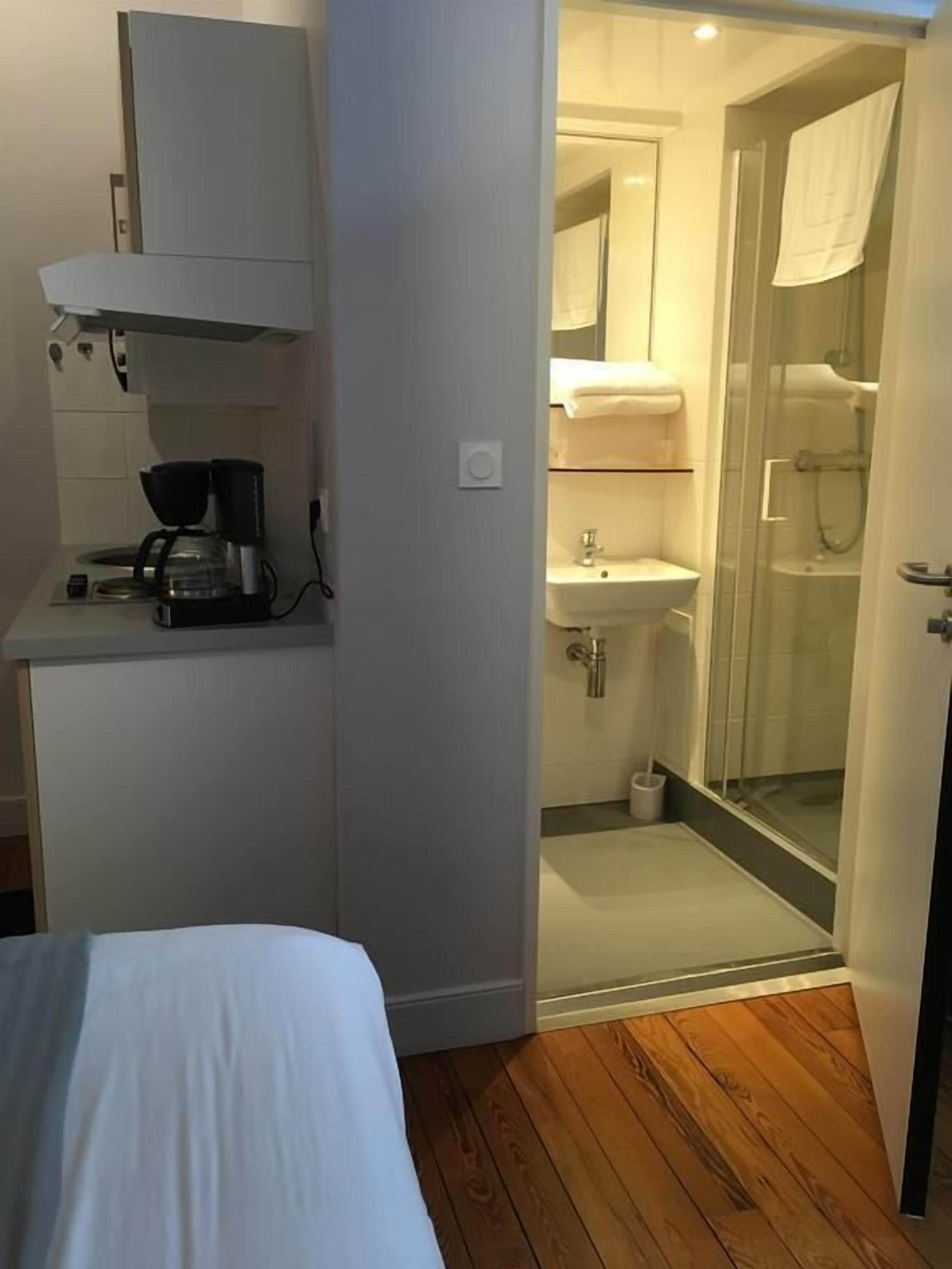 A bedroom with a bed, a coffee maker, and a small cabinet.