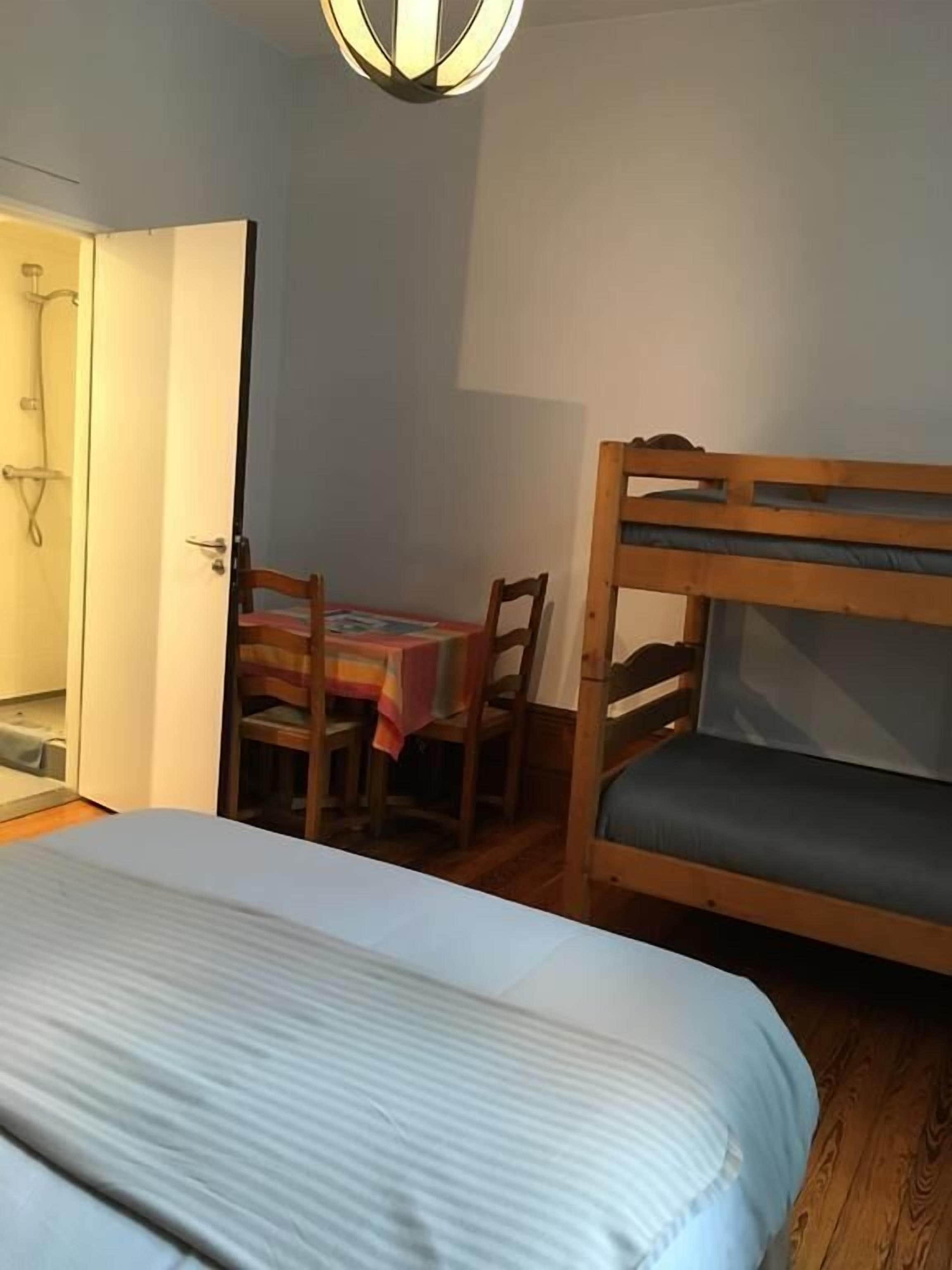 Una habitación con literas, una pequeña mesa con sillas y una puerta que da a un baño.
