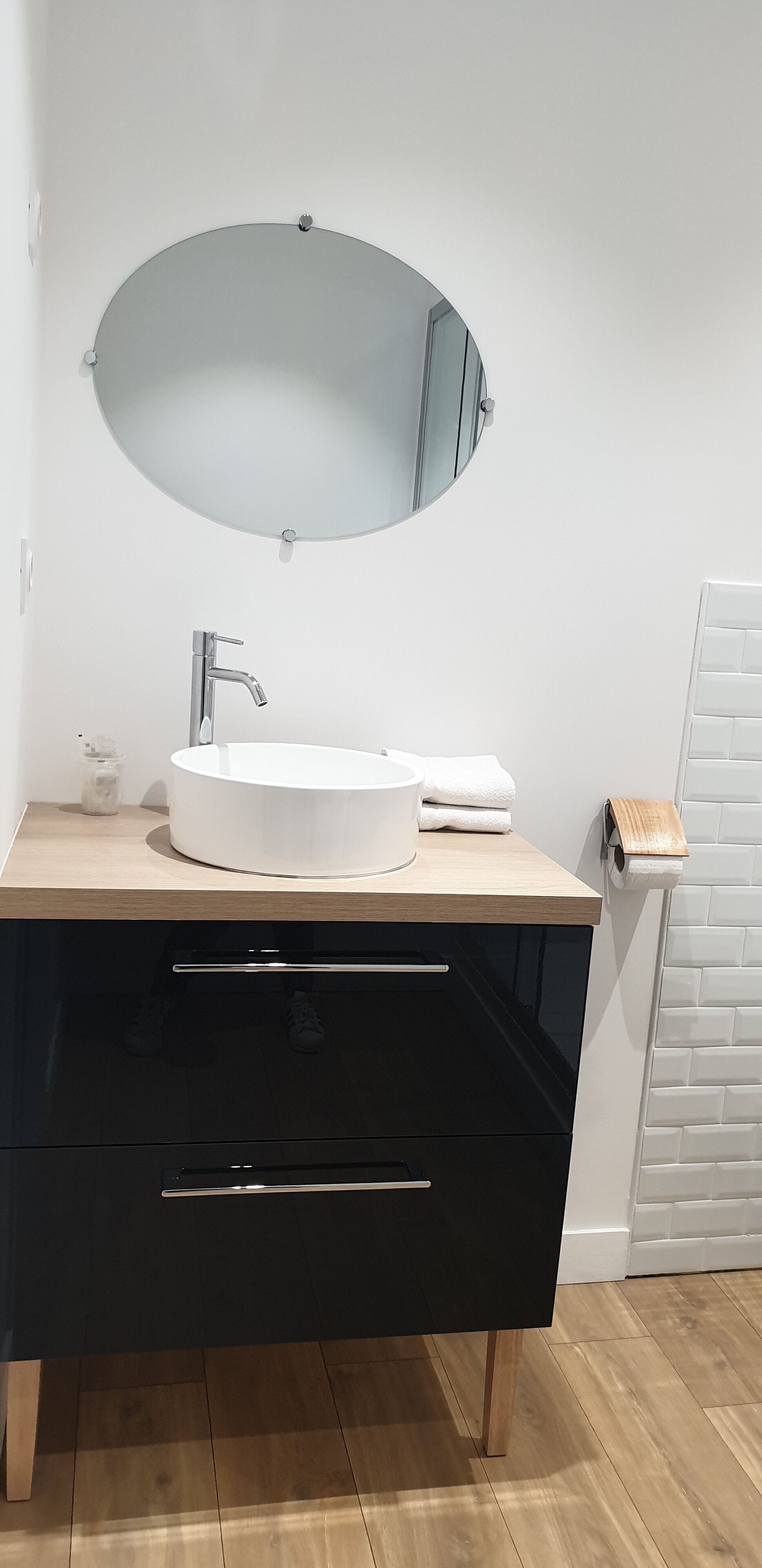 Un baño moderno con un lavabo blanco, un espejo redondo y un mueble de tocador negro con cajones.
