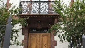 Un bâtiment doté d’une porte double en bois, d’un balcon orné de balustrades en fer forgé et d’un escalier en pierre menant à l’entrée.