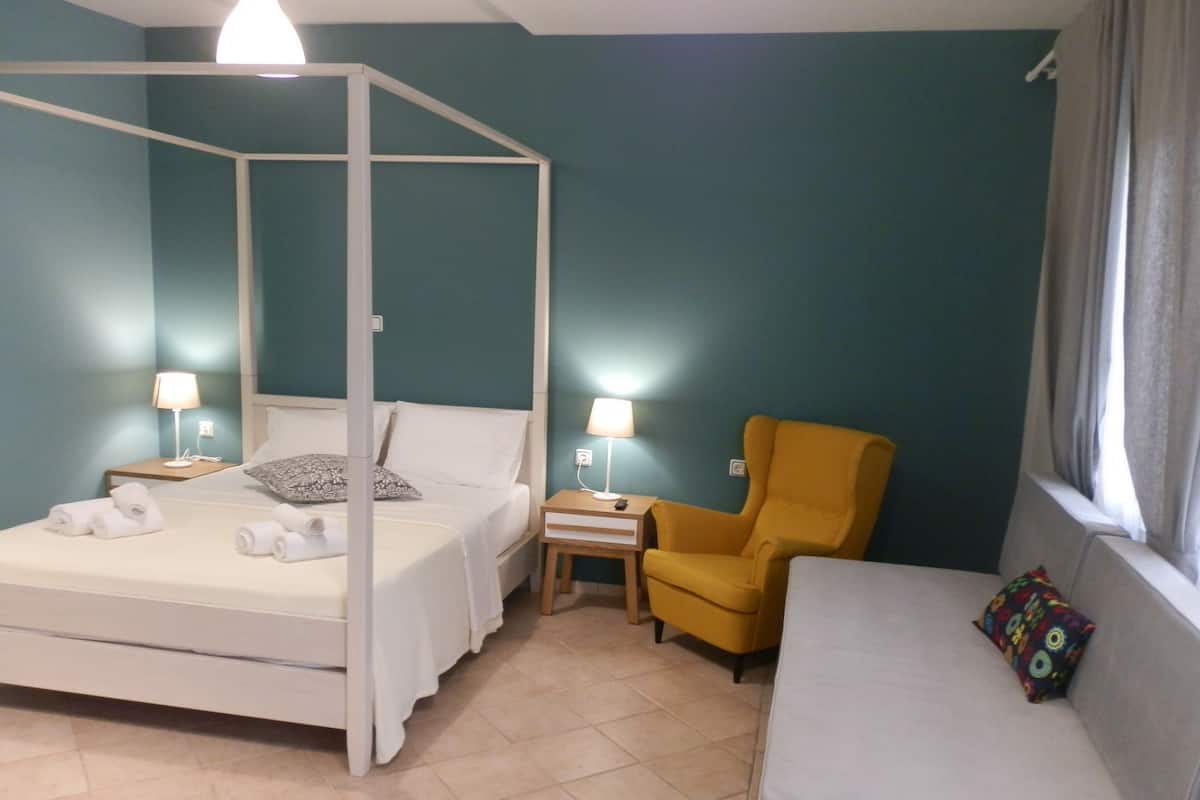 Quarto com cama de dossel, sofá, poltrona amarela e janela com cortinas.