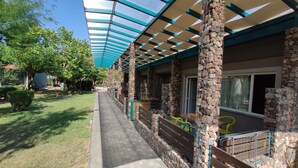 A covered outdoor seating area with stone pillars, a brick pathway, and a view of a residential building. - Philoxenia (Kalabaka)
