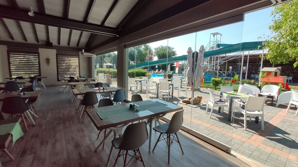An outdoor dining area with tables and chairs, a pool, and umbrellas. - Philoxenia (Kalabaka)