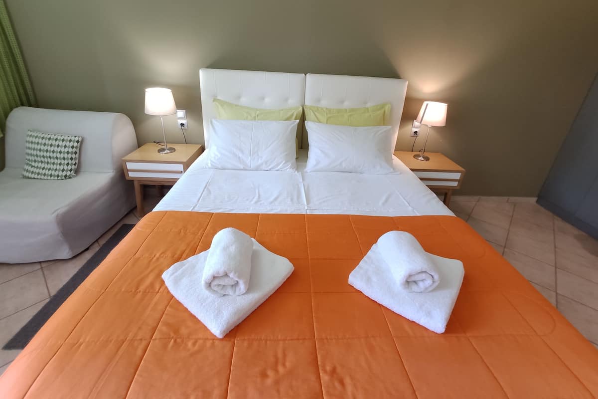 Quarto de hotel com cama, duas mesas de cabeceira, abajur, sofá e almofada estampada.