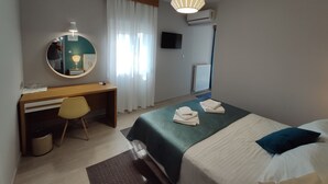 A hotel room with a bed, a desk, a chair, a round mirror, a hanging light fixture, and a television. - Philoxenia (Kalabaka)