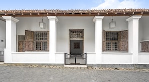 A building with a tiled roof, white columns, and wooden shutters on the windows.