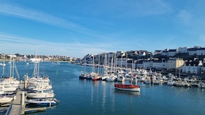 Un port de plaisance où sont amarrés différents types de bateaux, un ciel dégagé et des bâtiments en arrière-plan.