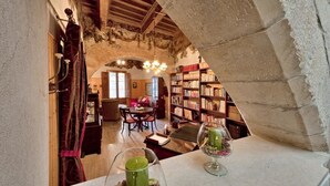 Un rincón acogedor para leer con un arco de piedra, una mesa de madera, sillas y una estantería llena de libros.