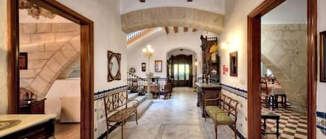 A spacious hallway with a checkered floor, wooden furniture, and a stone archway.