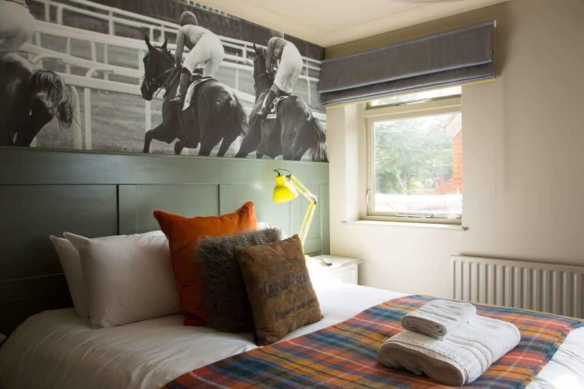 A hotel room with a bed, pillows, a blanket, a window with a view, and a wall-mounted lamp.