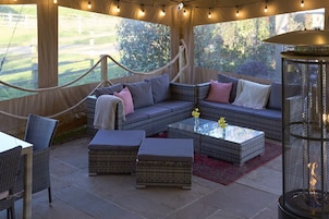 Un espace extérieur aménagé avec des meubles en osier, une table basse en verre et une vue sur un jardin.