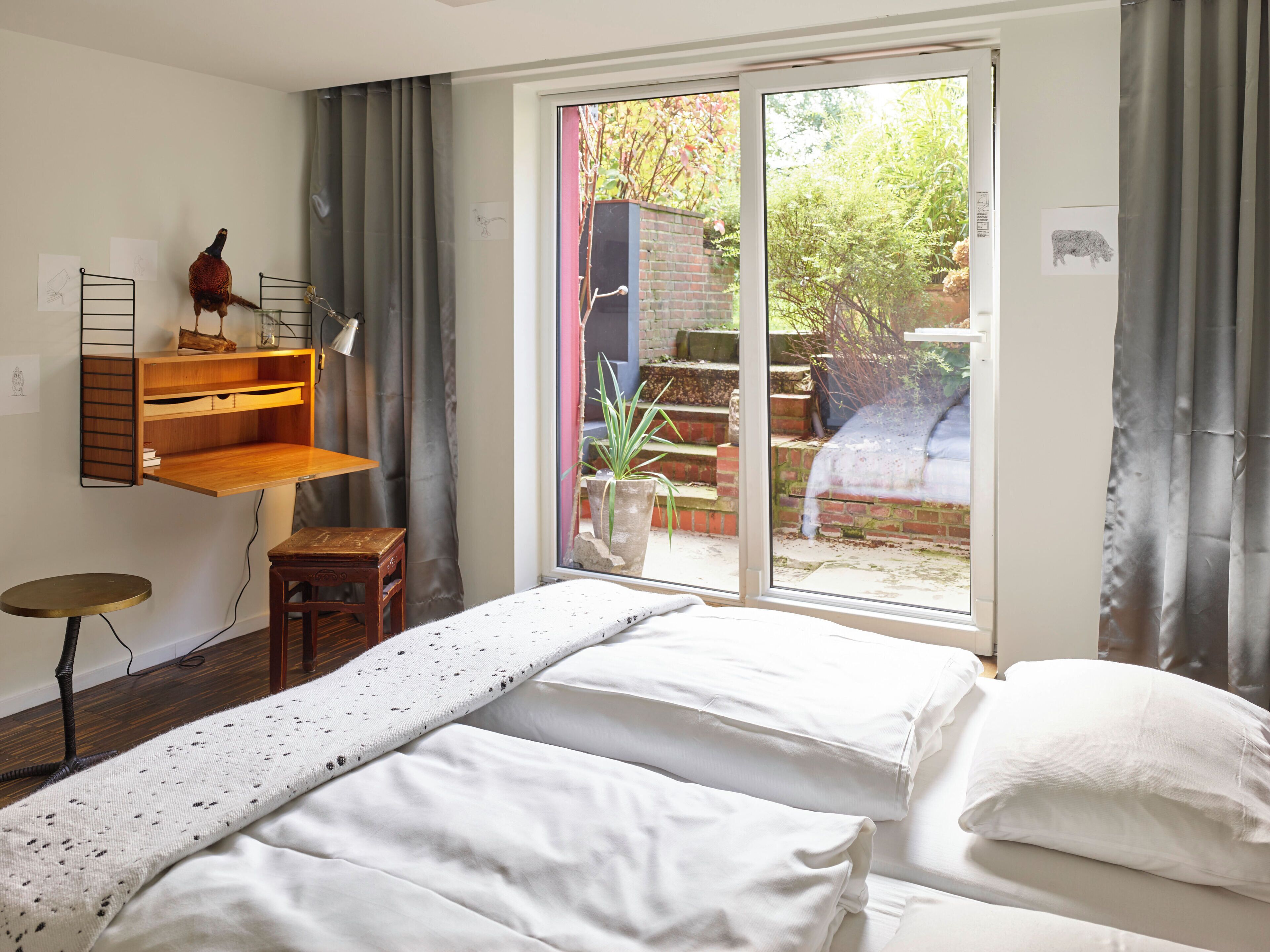 A bedroom with two beds, a desk, a chair, and a window with a view of a garden.