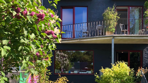 A modern two-story building with balconies, large windows, and a well-maintained garden with various plants and flowers. - Das kleine Schwarze (Hamburg)
