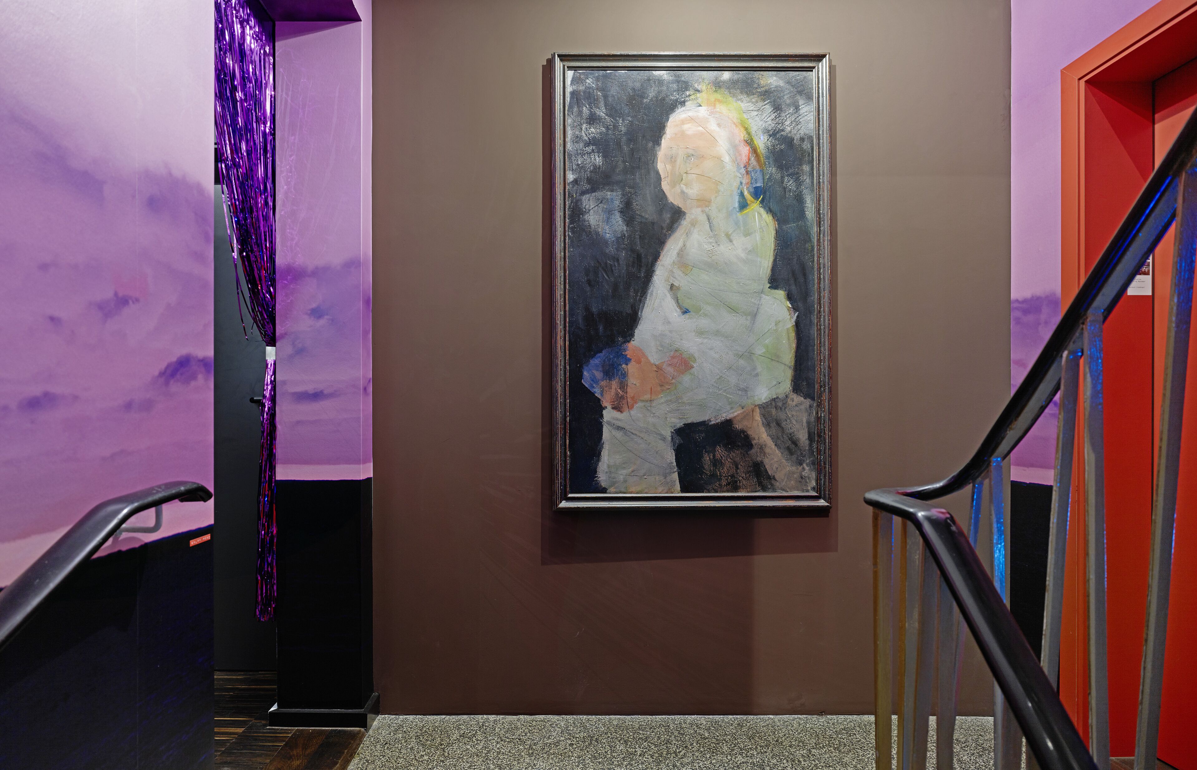 A hallway with a framed painting on the wall, a purple wall, and a staircase with a red railing.