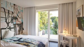 A modern hotel room with a large bed, a desk, and a balcony with a view of trees. - Das kleine Schwarze (Hamburg)