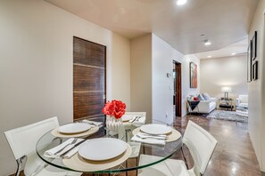 A modern dining area with a glass table, white chairs, and a vase with red flowers. - Mountain-View Patio: Sedona Suite Near Trails (Sedona)