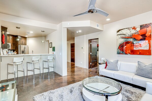 A modern kitchen with white appliances, a bar area with white bar stools, a white sofa with grey cushions, and a glass coffee table. - Mountain-View Patio: Sedona Suite Near Trails (Sedona)