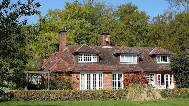 A traditional brick house with a pitched roof, multiple chimneys, and white-framed windows. - Grandwood House (Chichester)